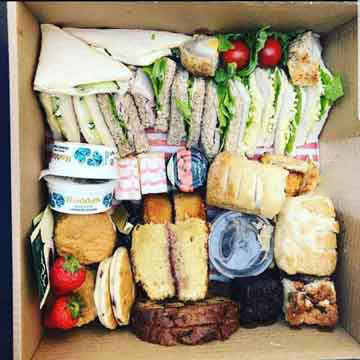 overhead view of afternoon tea box with cakes, scones, jam and cream and sandwiches